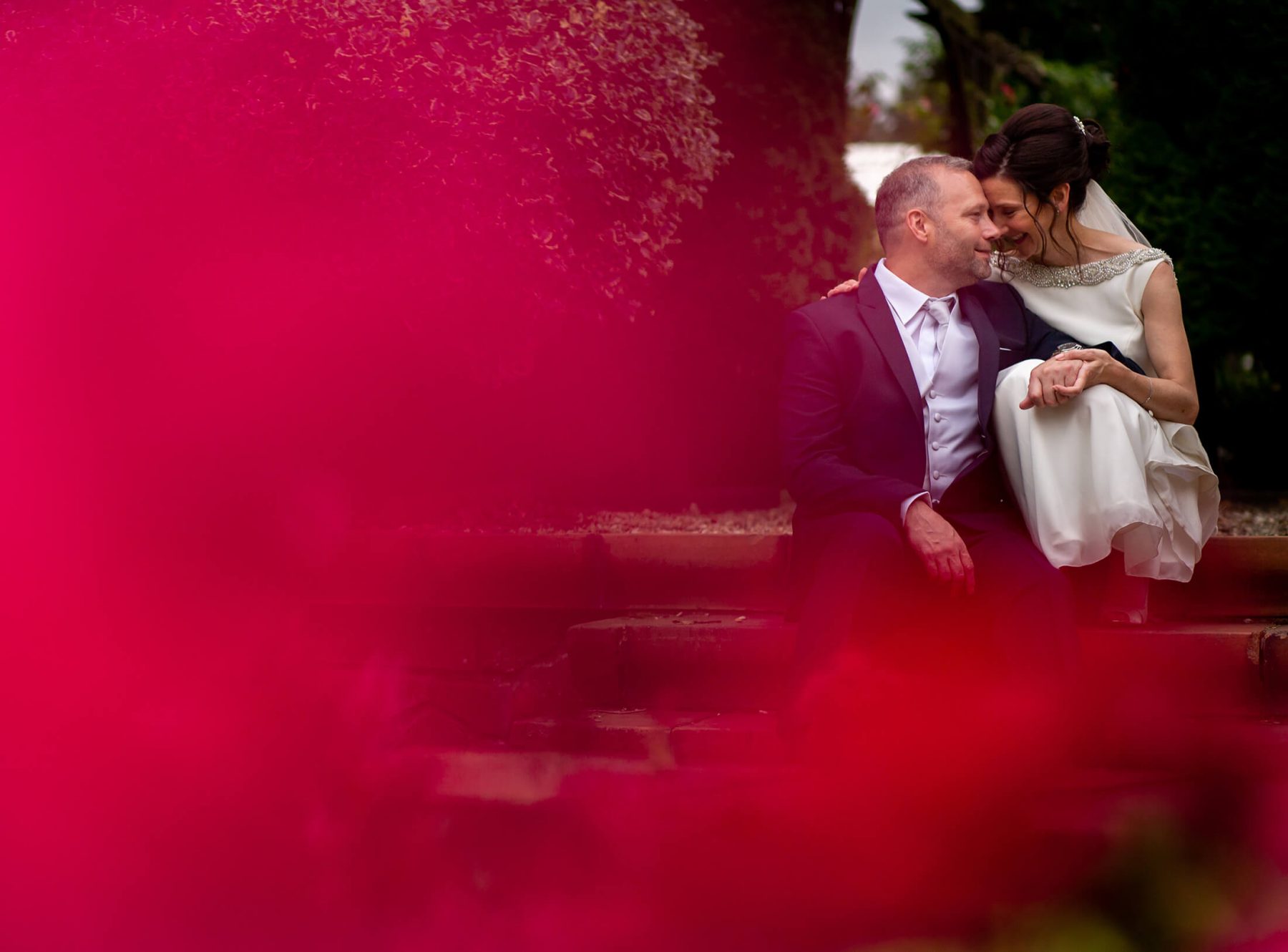 The Bride and groom sit on the steps in the gardens.