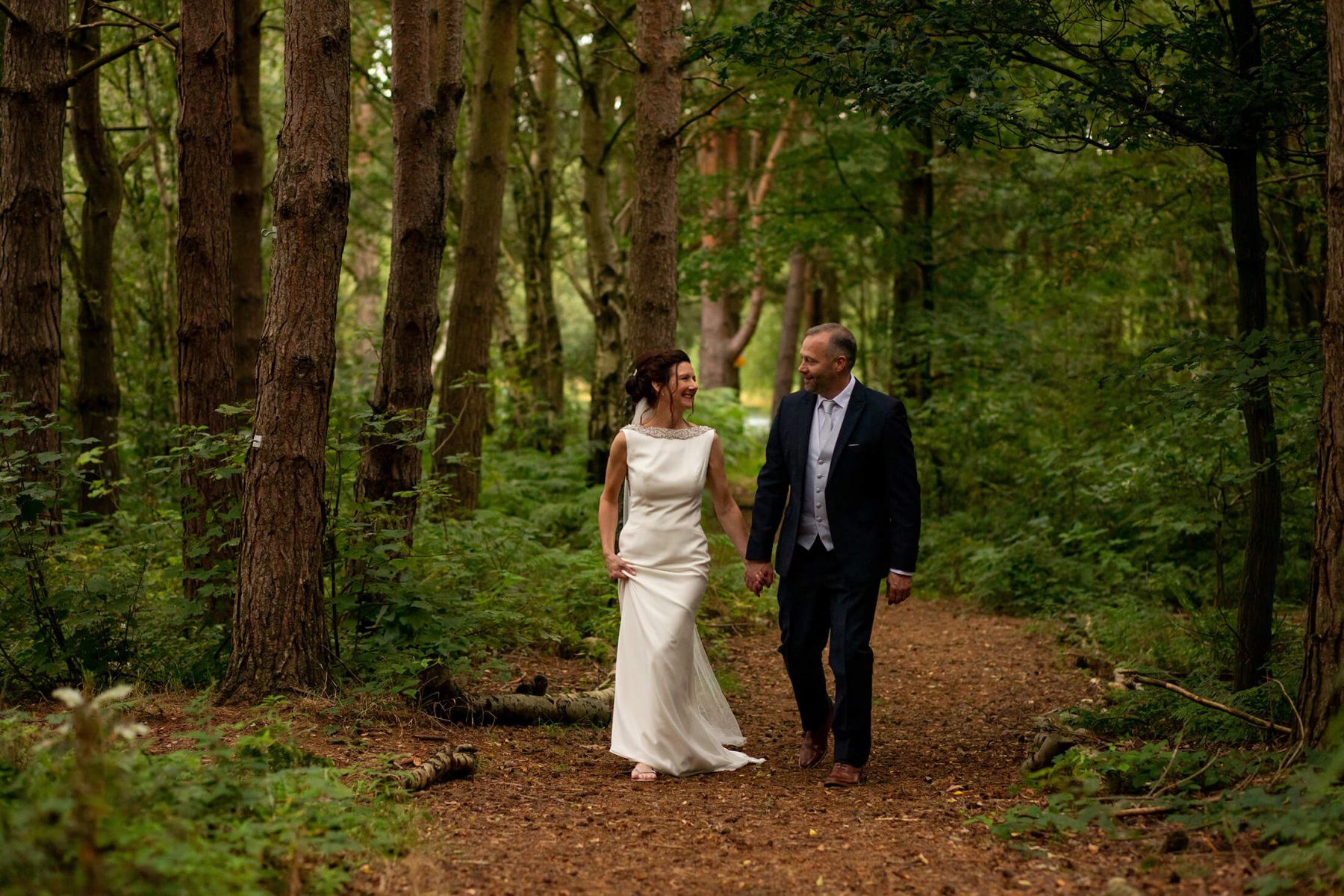 The bride and groom walk through the woods.