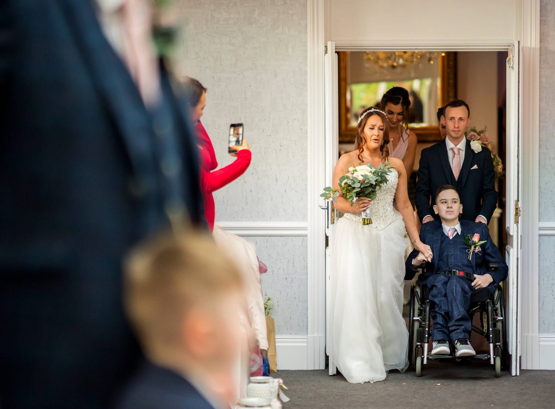 Hollin Hall Hotel Wedding Photographer - The bride is led down the aisle by her son in his wheelchair.