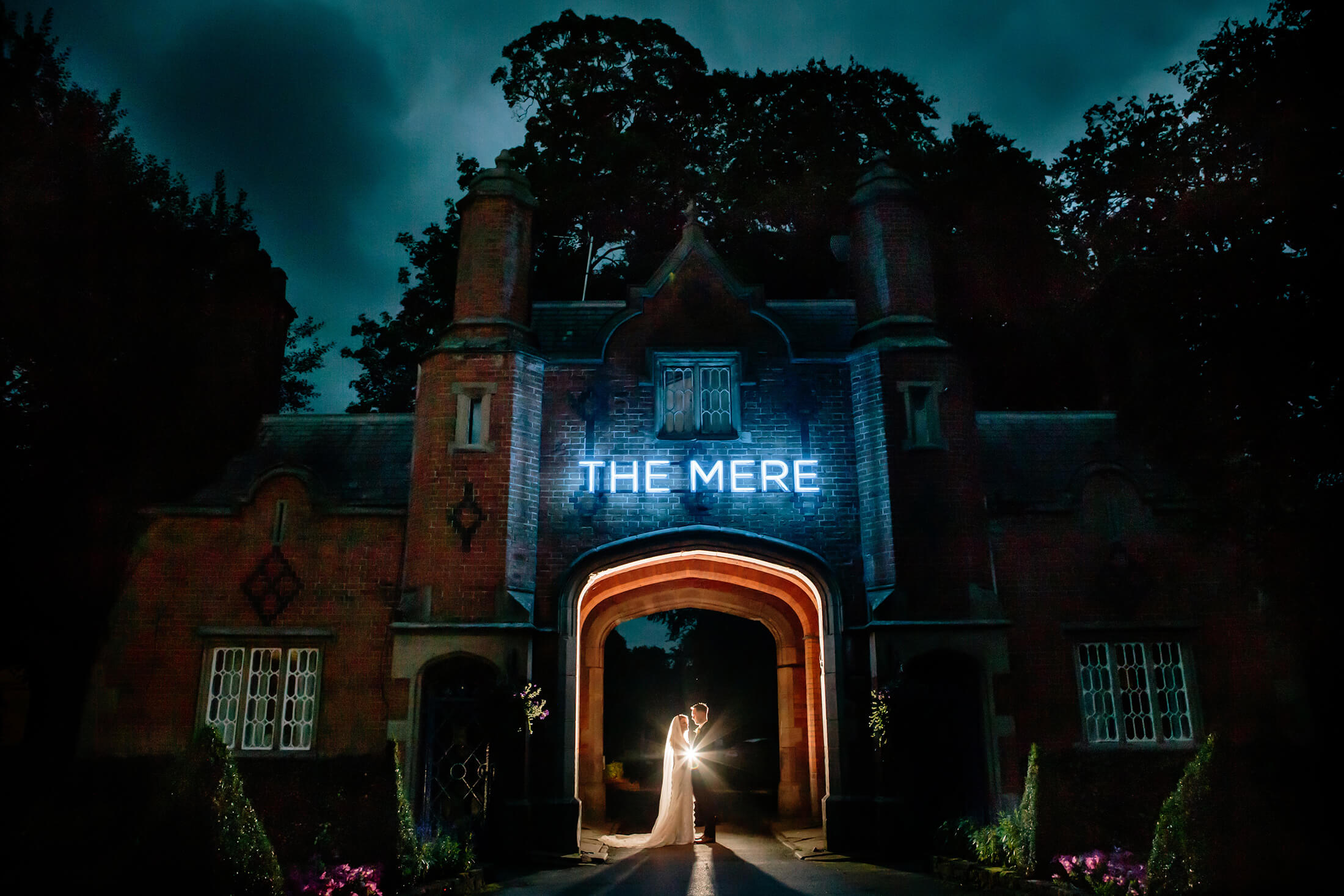A night time portrait of the bride and groom under the arch at the Mere Golf Resort & Spa in Cheshire. Mere Resort Wedding Photographer