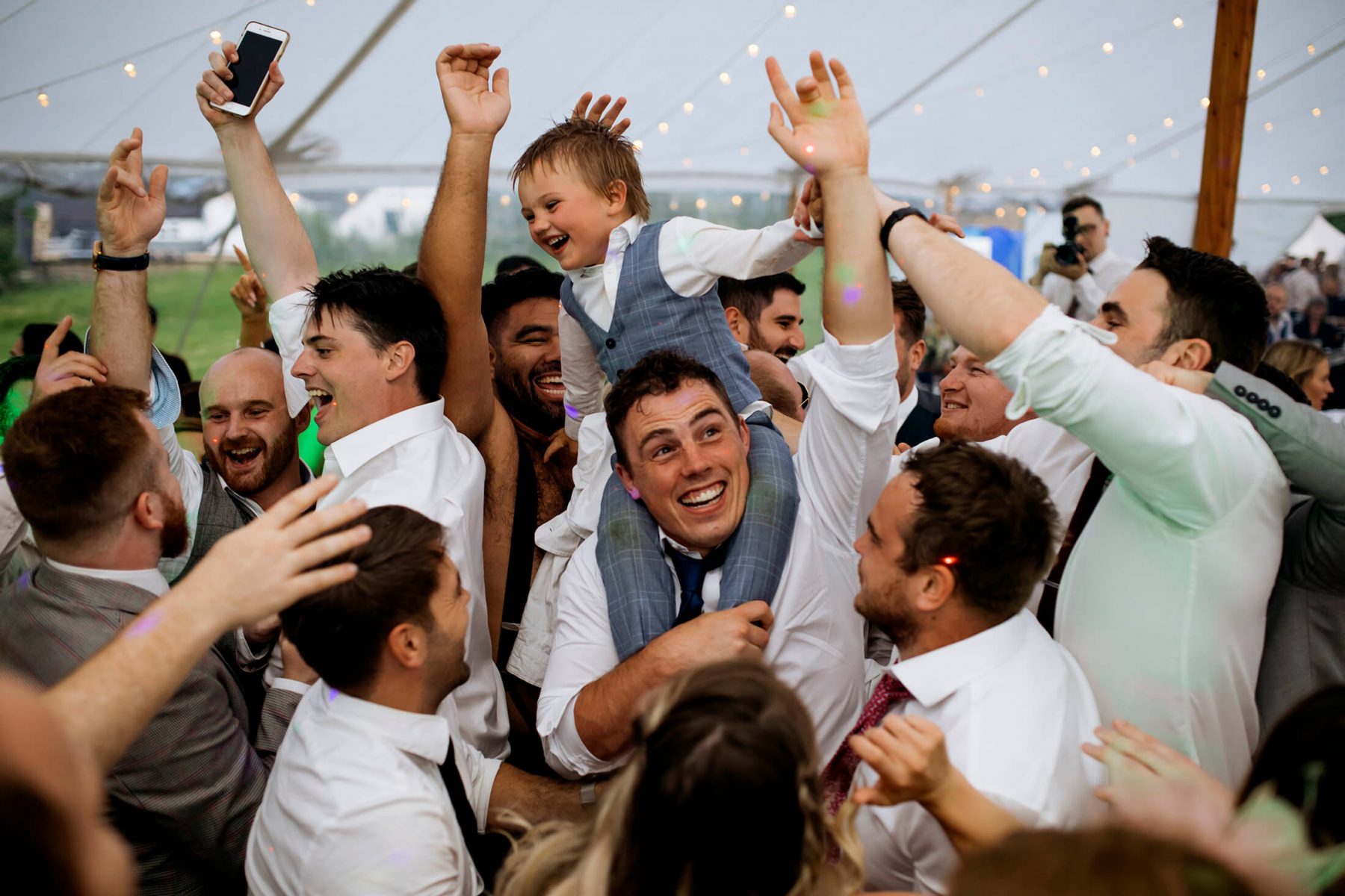 A young boy is lofted onto a mans shoulders on the dancefloor during the wedding party. Staffordshire Wedding Photographer