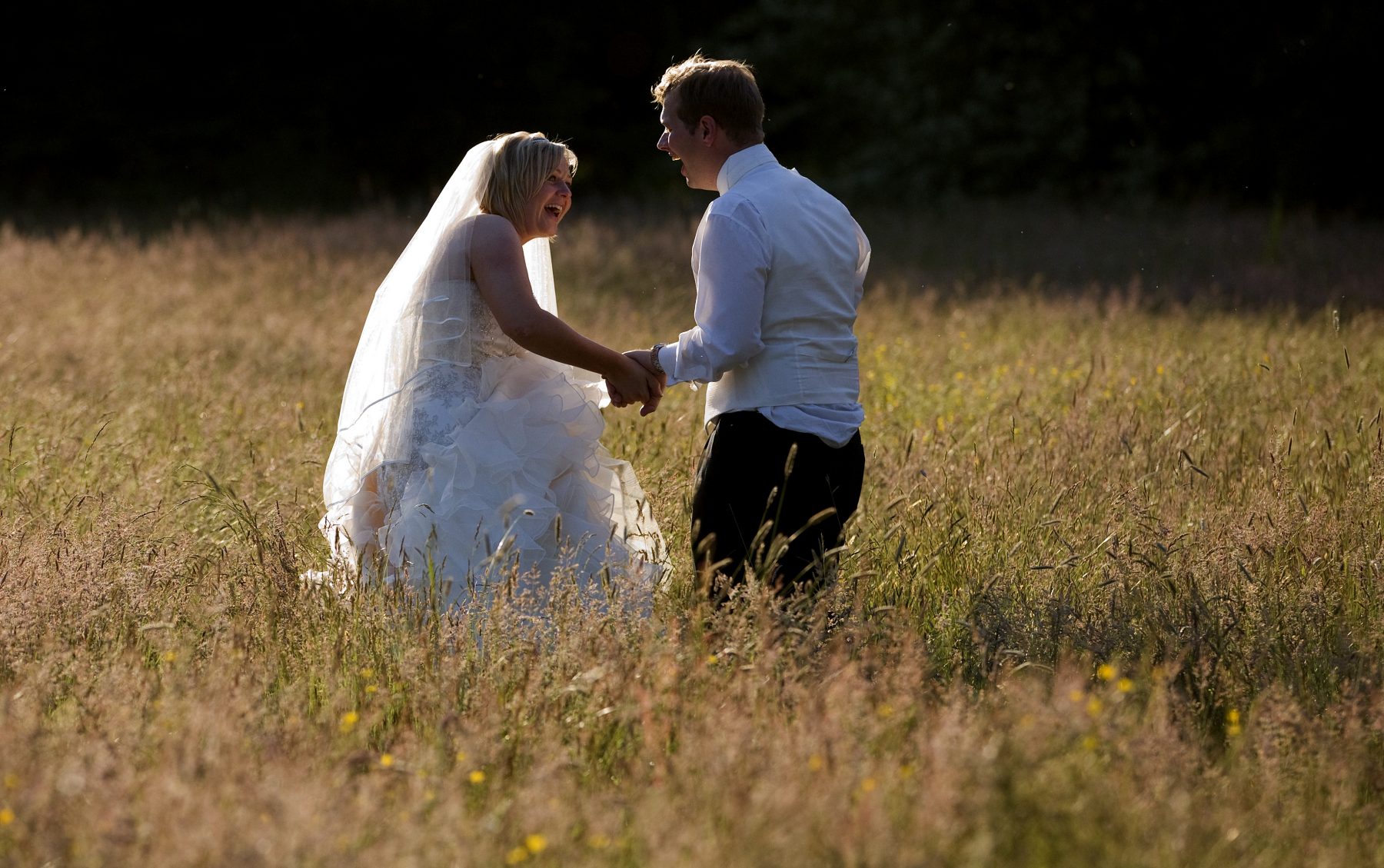 A bride and groom laugh during an evening sunset walk in the long grass after their wedding at Iscoyd Park in Shropshire.