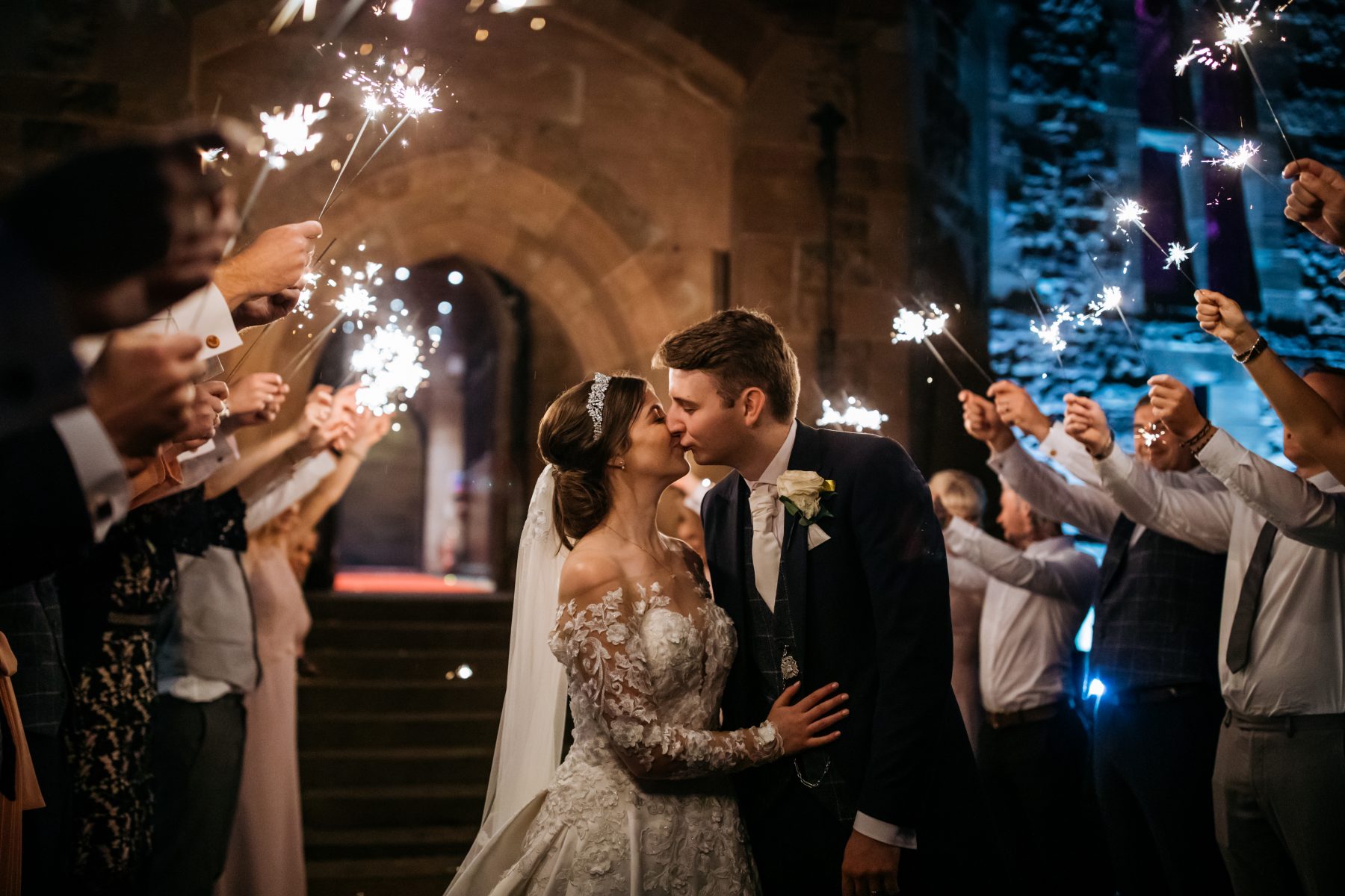 A bride and groom stand beneath sparklers supplied by their photographer after their wedding at Peckforton Castle in Cheshire.