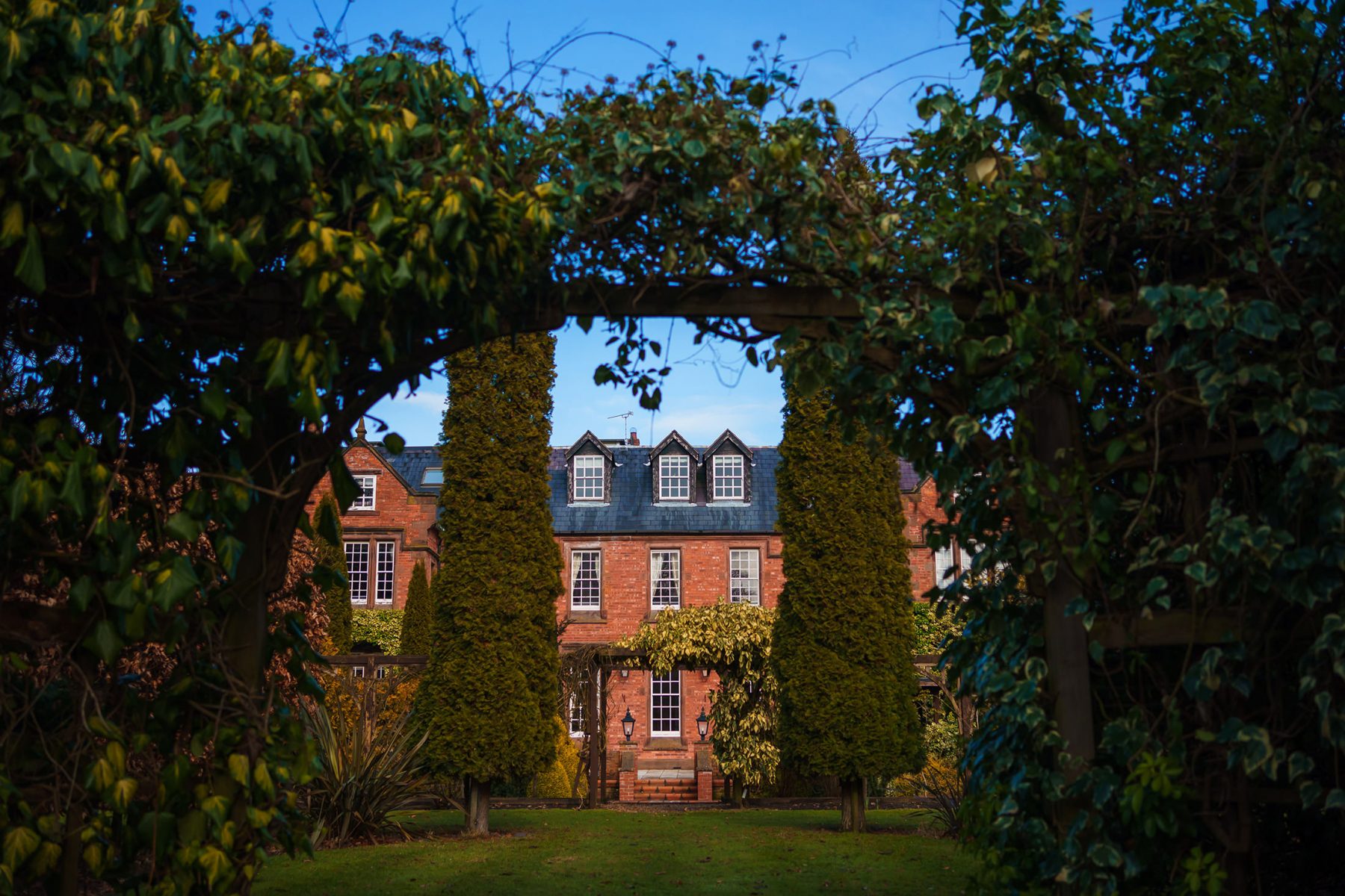 A photograph main building through an archway in the gardens at Nunsmere Hall in Cheshire - Country House weddings at Nunsmere Hall