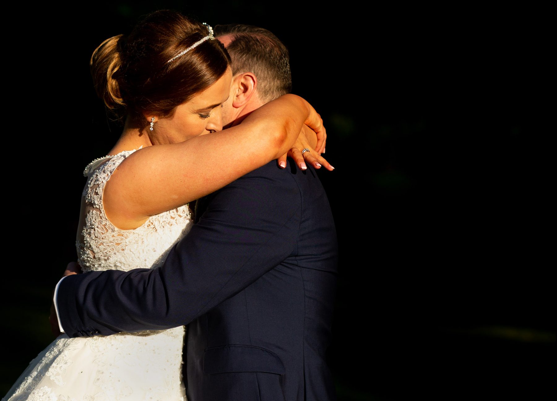 The bride hugs her groom in evening sunlight after thier wedding ceremony