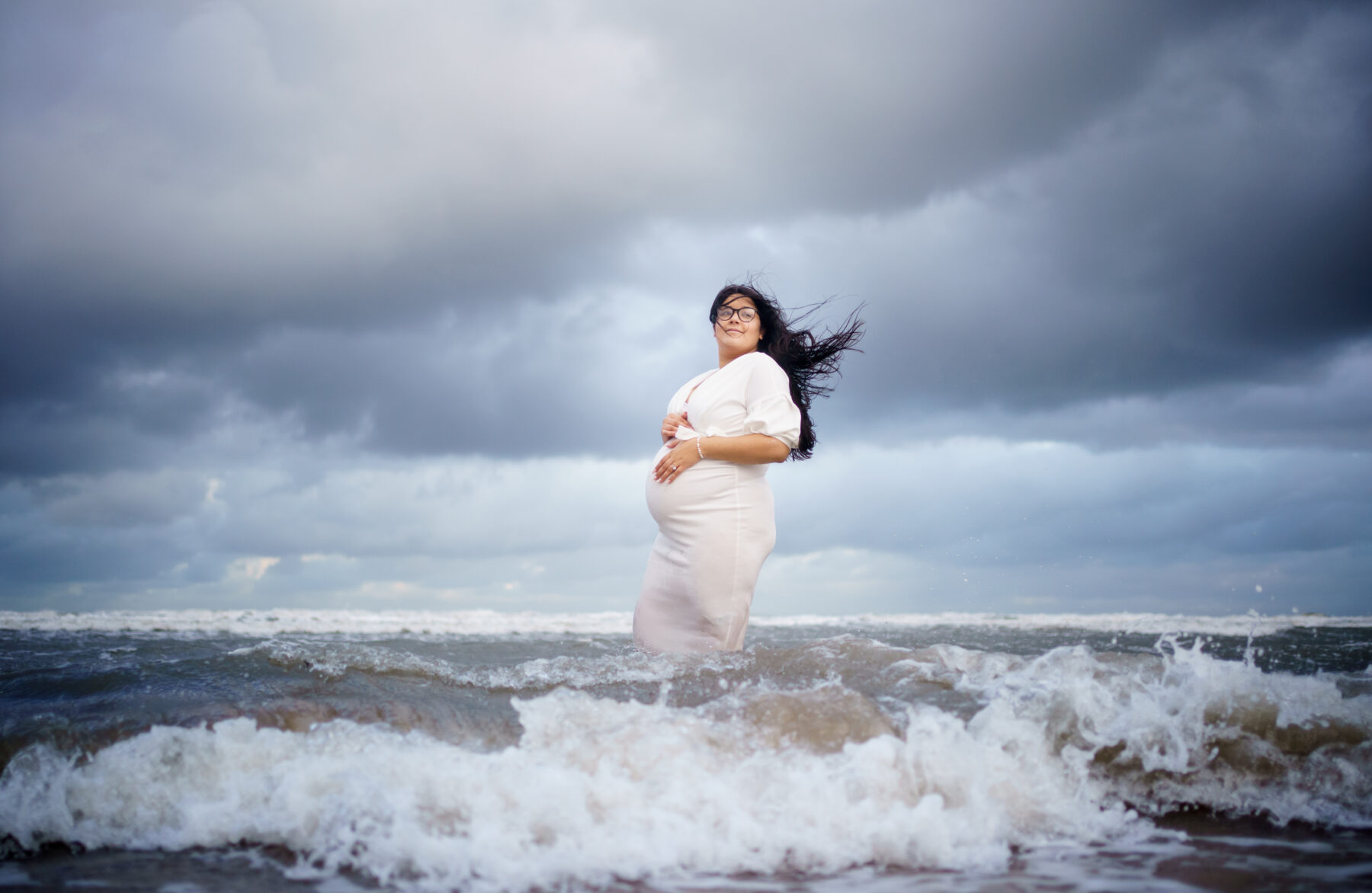 A pregnant woman stands in the sea.
